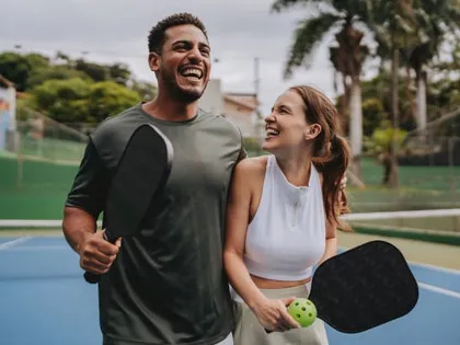 Hai người chơi cười vui trên sân pickleball ngoài trời, tay cầm vợt.
