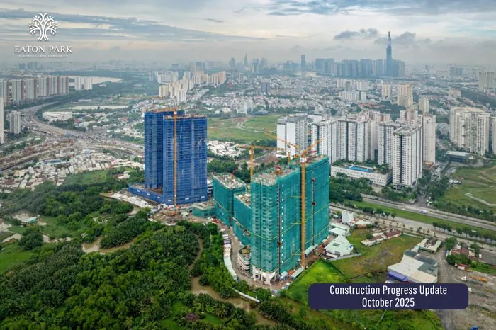 Aerial photograph of Eaton Park in October 2025. Strait and Grove are rising under blue netting to the left, the green-netted towers are climbing with tower cranes in place, and the city skyline stands behind.