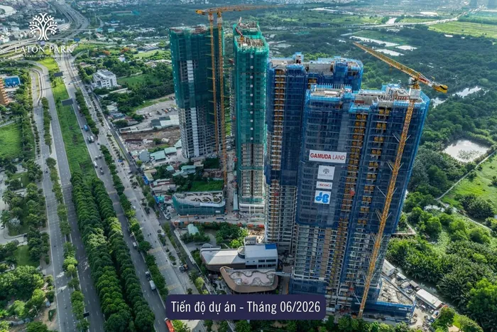 Ảnh chụp tiến độ Eaton Park từ trên cao, tháng 6 năm 2026. Các tòa tháp đã đạt chiều cao thiết kế dưới lưới bao che xanh lá và xanh dương, cần cẩu tháp còn tại chỗ, khối đế và cảnh quan đang hình thành.